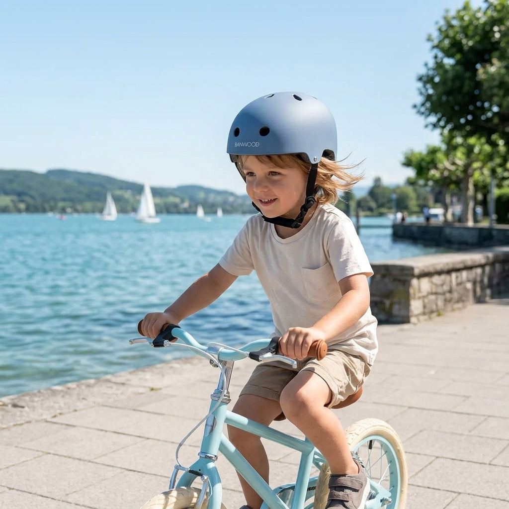 Child cycling along a lakeside promenade wearing the Banwood Classic Helmet in matte blue