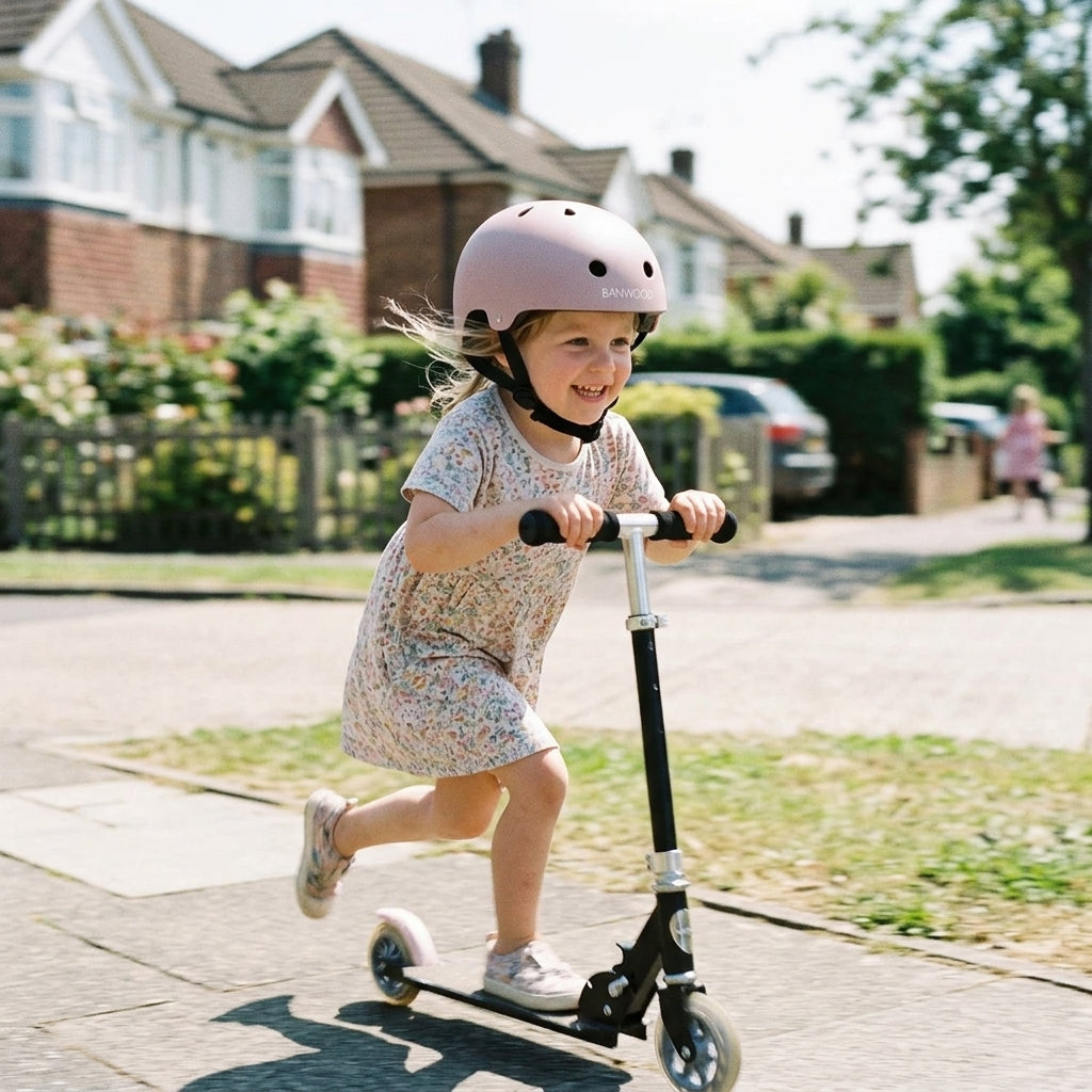 Child riding a scooter outdoors wearing the Banwood Classic Helmet in matte dusty pink