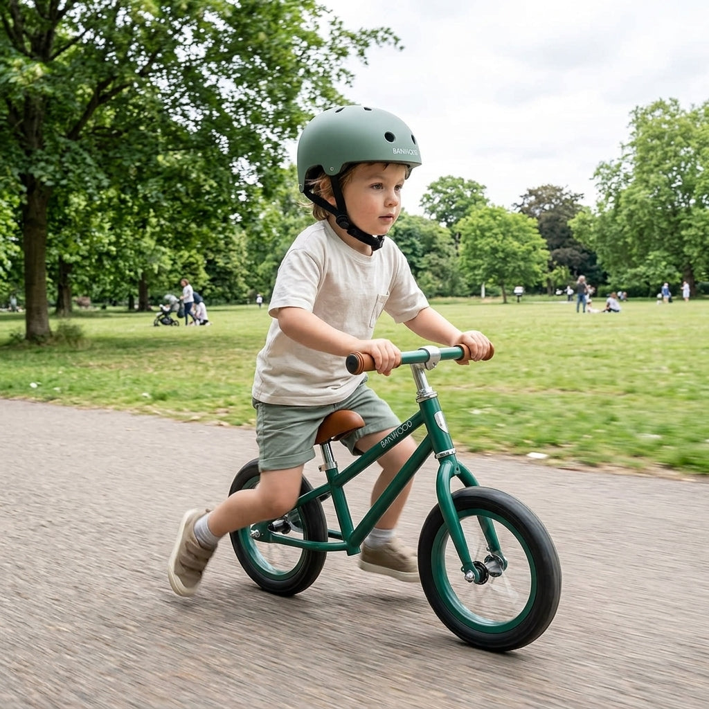 Child riding a balance bike outdoors wearing the Banwood Classic Helmet in matte forest green