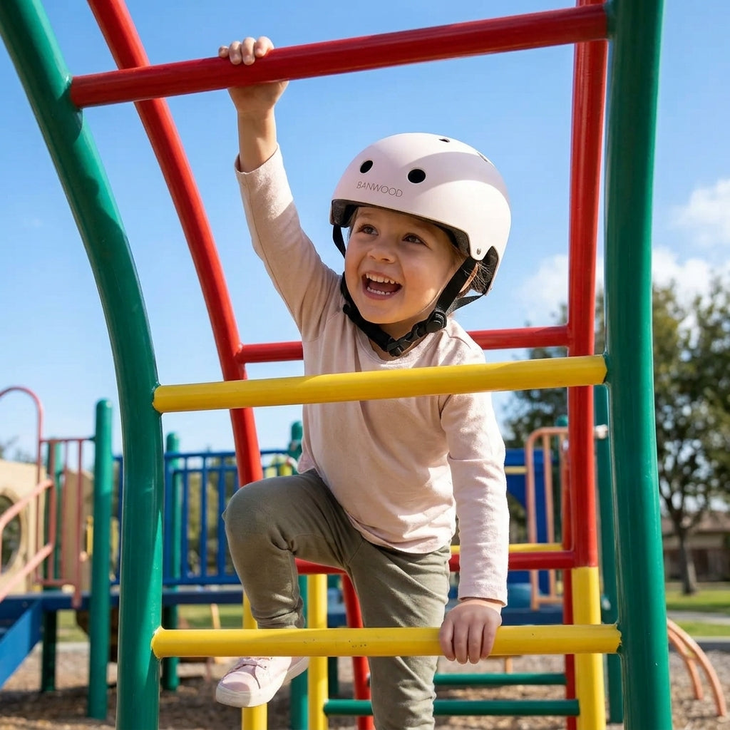 Child climbing a playground frame outdoors wearing the Banwood Classic Helmet in matte pink