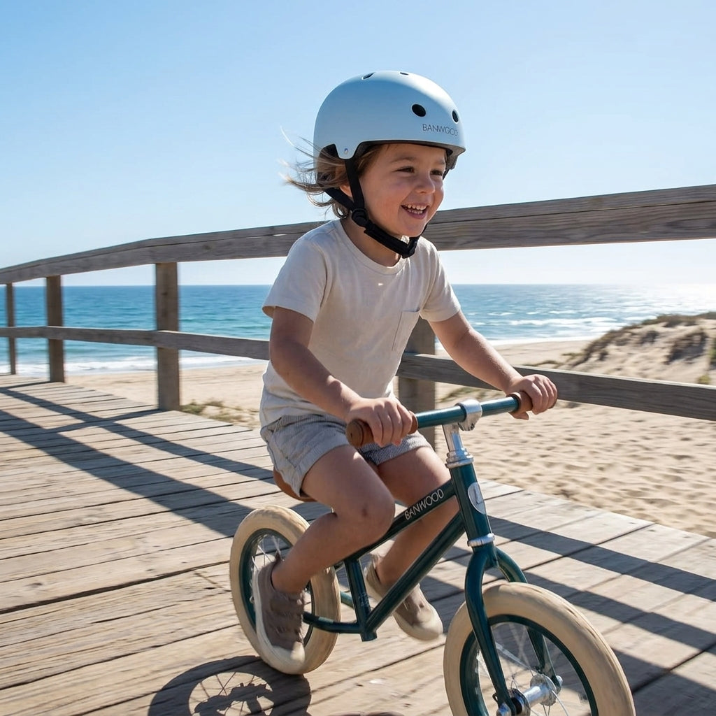 Child cycling along a seaside boardwalk wearing the Banwood Classic Helmet in matte sky blue