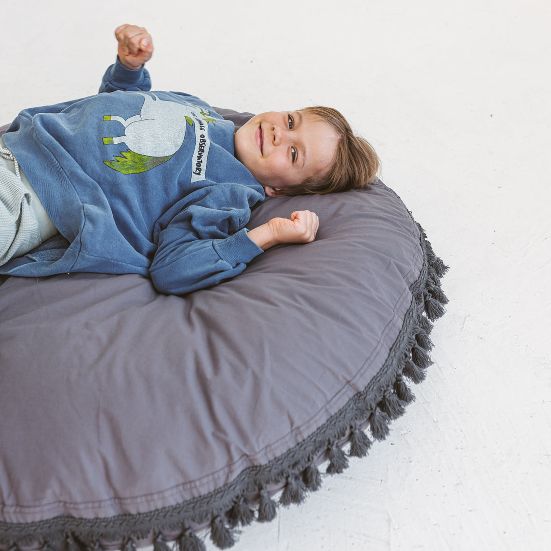 Child lying on the MINICAMP grey floor cushion with arms stretched overhead
