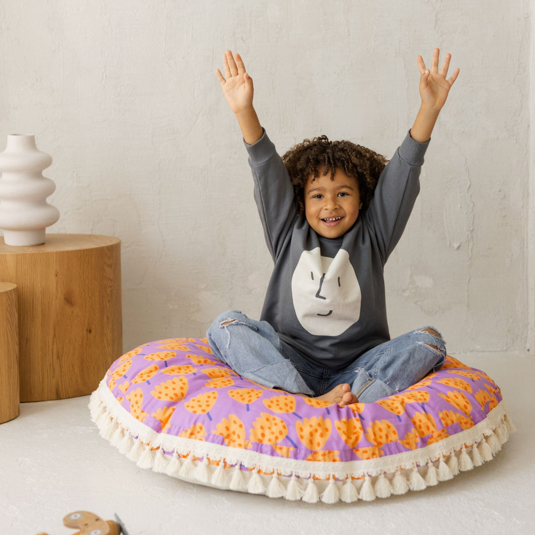 Child kneeling on the MINICAMP tulip print floor cushion with arms raised