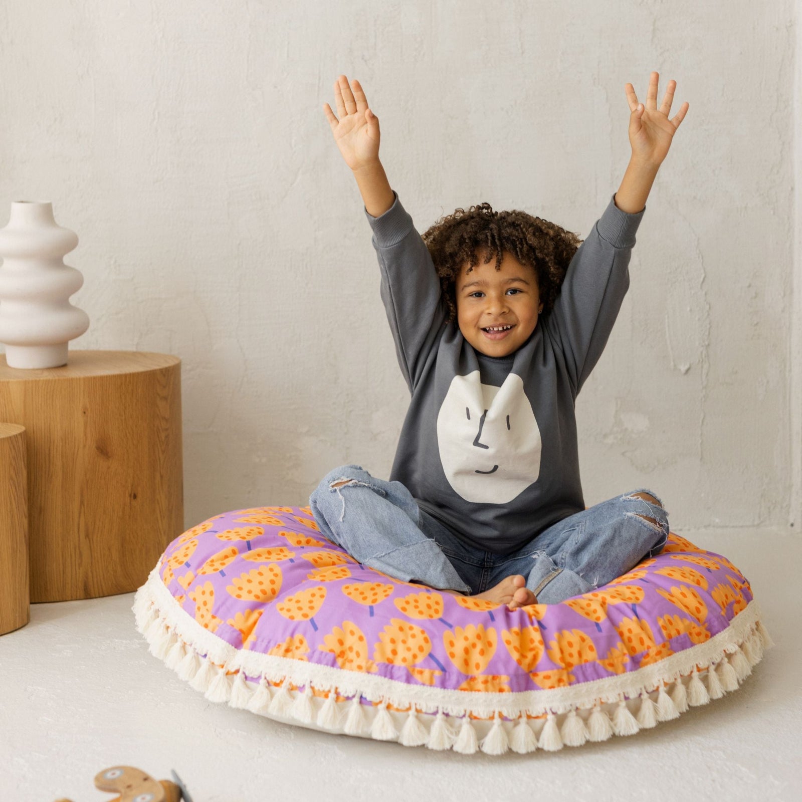 Child kneeling on the MINICAMP tulip print floor cushion with arms raised