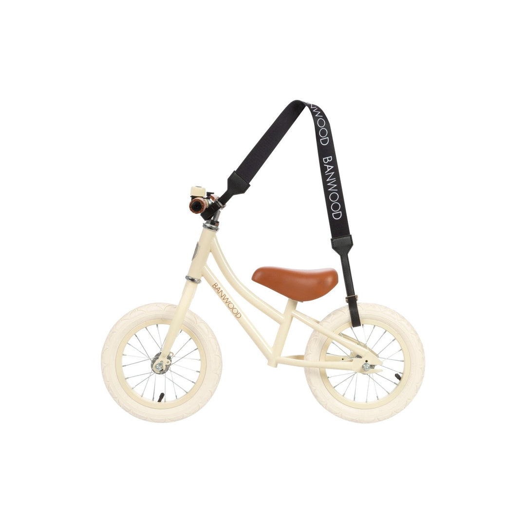 Black carry strap mounted on cream balance bike showing attachment mechanism