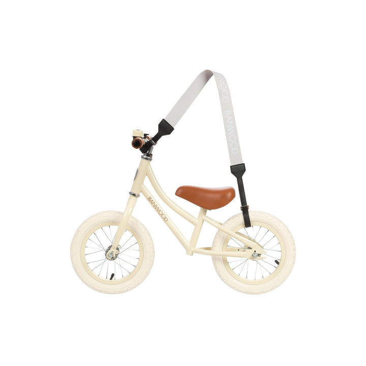 Cream balance bike suspended from carry strap showing hook attachment point