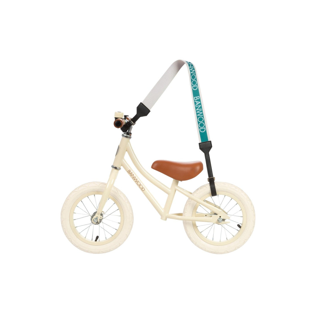 Adult wearing teal carry strap across body with cream balance bike, Banwood