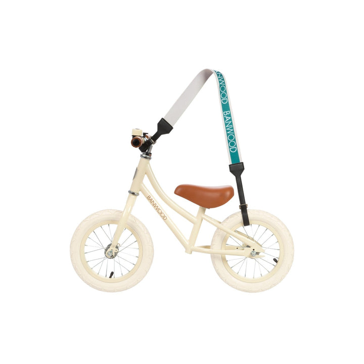 Adult wearing teal carry strap across body with cream balance bike, Banwood