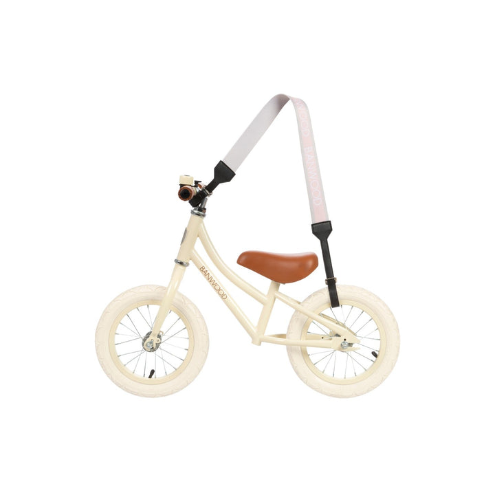 Cream balance bike with pink carry strap in use, side view