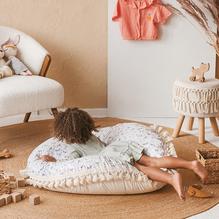 Child resting on the MINICAMP forest animal print floor cushion in a cosy playroom corner