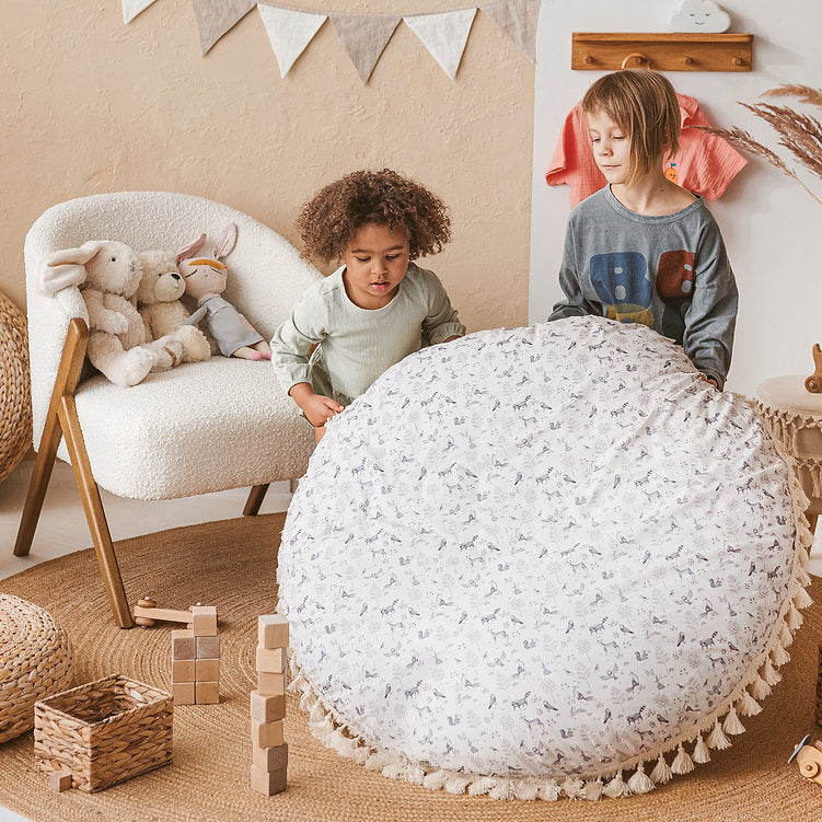 Two children kneeling beside the MINICAMP forest animal print floor cushion, looking closely at the printed pattern
