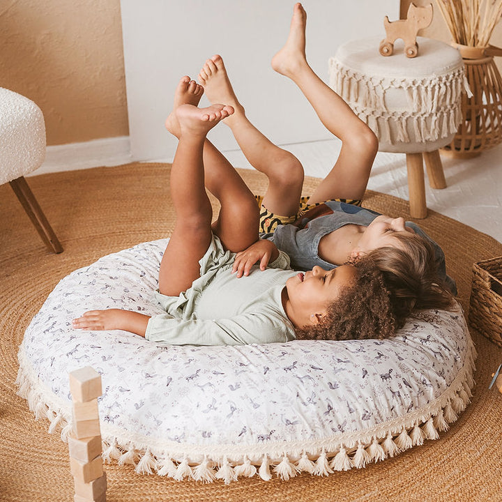 Two children lying together laughing on the MINICAMP forest animal print floor cushion
