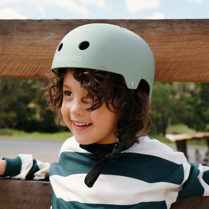 Child wearing pale green Banwood helmet in outdoor garden setting, side profile