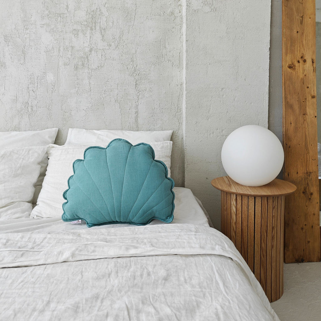 Mint linen seashell cushion resting on a bed against white linen pillows