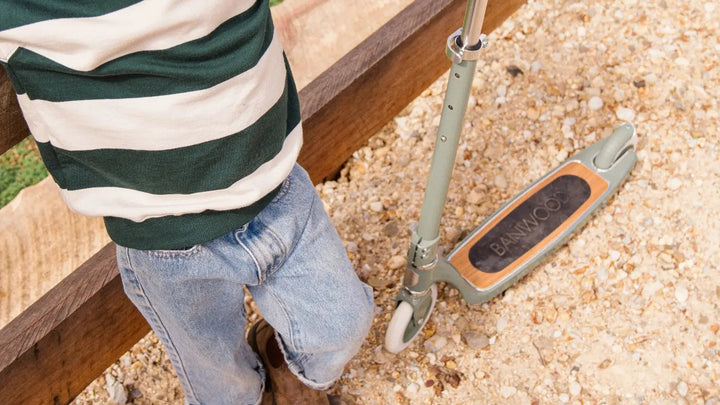 Child riding Banwood scooter on sandy beach in striped top