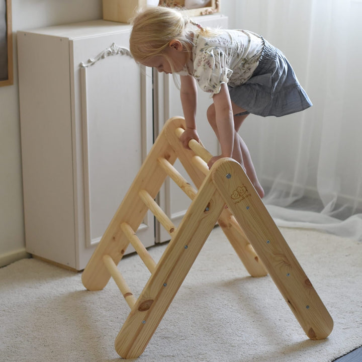 Young girl climbing over the top of the natural wood MeowBaby triangle ladder, used on its own without the board