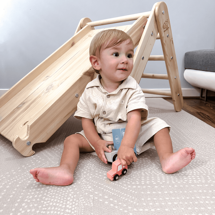 Toddler sitting on a play mat in front of the MeowBaby natural wood triangle ladder with the slide attached