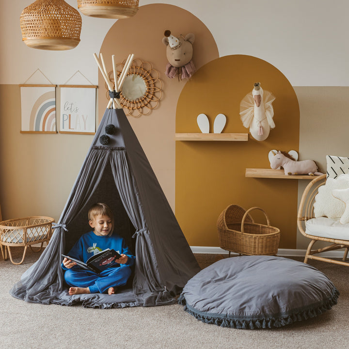 The MINICAMP grey floor cushion beside a play teepee, with a child reading inside the teepee