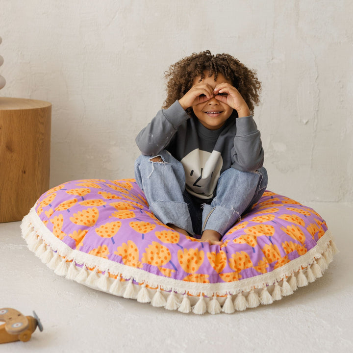 Child playing peekaboo while sitting on the MINICAMP tulip print floor cushion