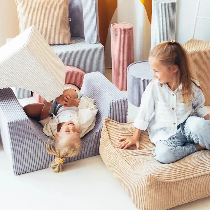 Two children playing on Wigiwama corduroy play sofa pieces in soft lilac, pink and sand tones
