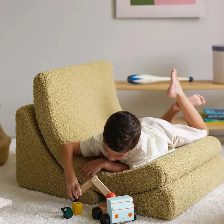 Boy lying across an olive textured Wigiwama children's chair, playing with a wooden toy truck
