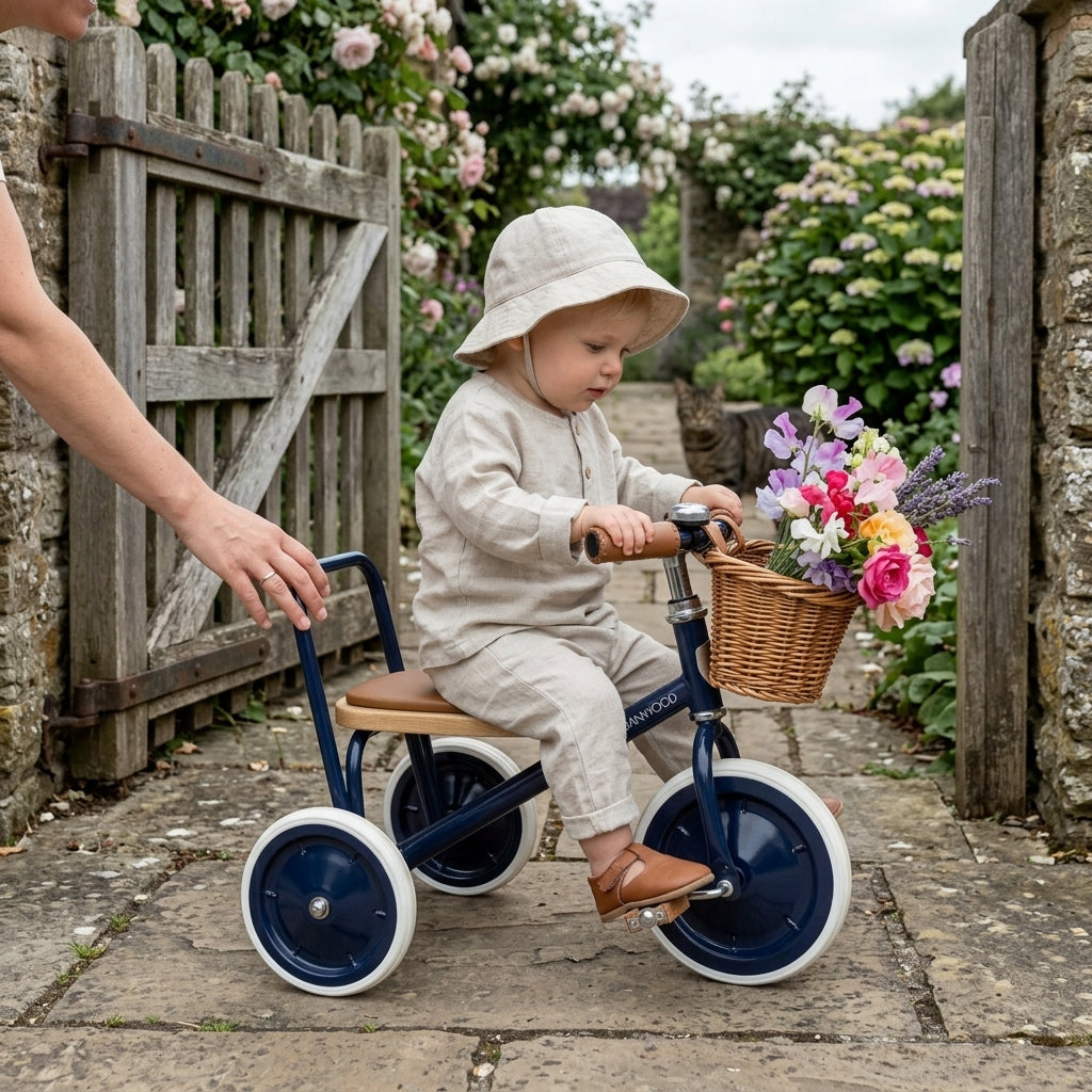 Toddler on the Banwood Trike Vintage in Navy near a garden gate with flowers in the basket