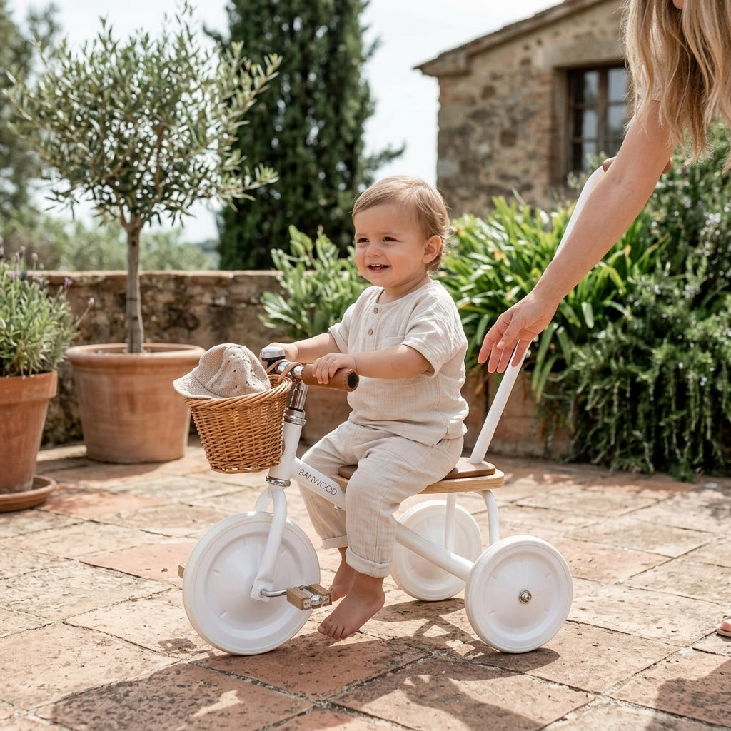 Toddler sitting on the Banwood Trike Vintage in White on a sunlit terrace with a parent guiding the push handle