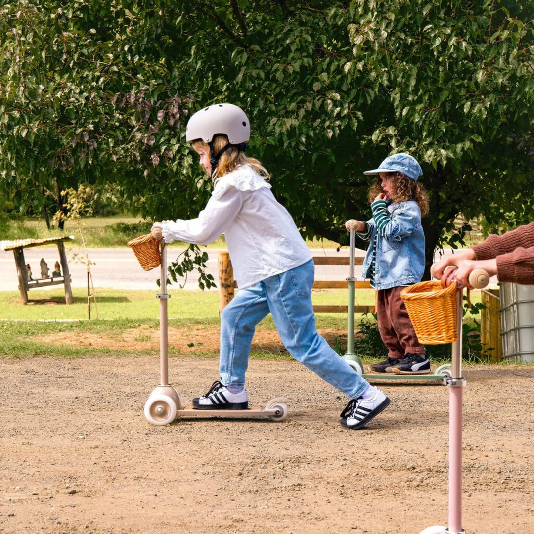 Child riding beige scooter with basket in outdoor park setting