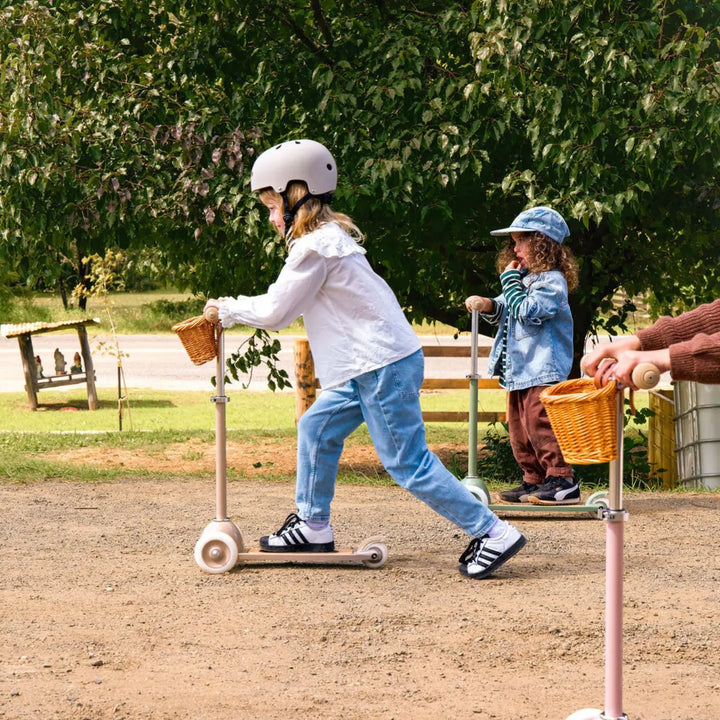 Child riding beige scooter with basket in outdoor park setting