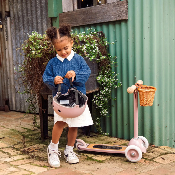 Child riding dusty pink Banwood scooter whilst carrying wicker basket